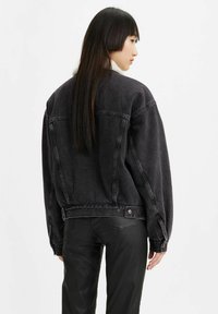 Giubbotto in denim nero con vestibilità rilassata, dotato di un collo in shearling. I dettagli includono chiusure a bottoni e orlo leggermente accorciato.