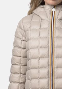 Giacca imbottita trapuntata beige con cappuccio, dotata di una cerniera multicolore e finitura testurizzata. Motivo a quadrati con microcuciture visibili.