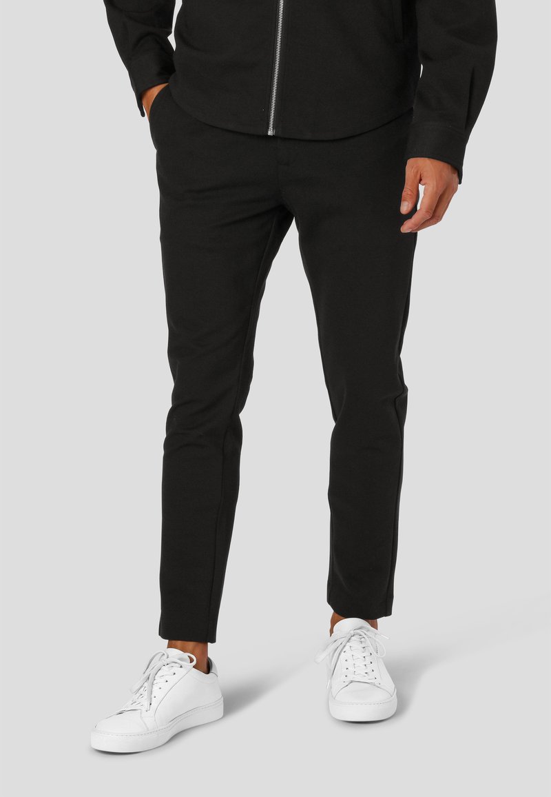 Črne slim-fit hlače iz mehke tkanine z gladko teksturo in čistim dizajnom, v kombinaciji z belimi supergami.