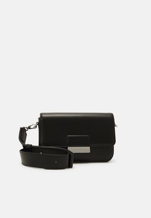 Sac bandoulière rectangulaire en cuir noir avec une large sangle réglable et une plaque logo Calvin Klein argentée sur le rabat avant.