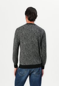 Siv sweater z značilnim ponavljajočim se potiskom "Guess Los Angeles", z rebrastimi manšetami in robom. Zadnji pogled prikazuje klasičen kroj s krožnim izrezom.