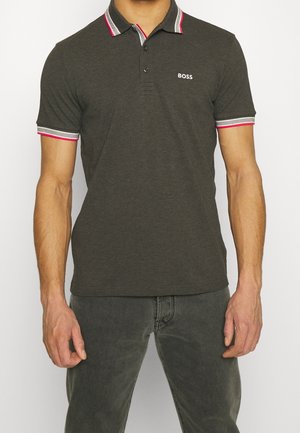 Mann trägt dunkelgraues Polohemd mit rosa-weiß gestreiftem Kragen und Ärmeln, "BOSS"-Logo auf der Brust, kombiniert mit dunkelgrauen Jeans.