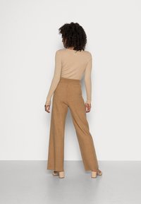 Beige geribbelde langemouwtop gecombineerd met hooggewijze, wijde tanbroek. Schoenen met een flinke hak. Soepele texturen, minimale detailing.