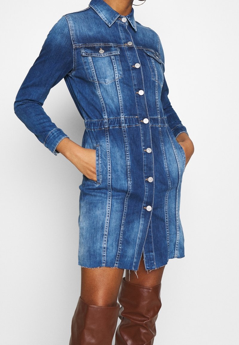 Jeansklänning med krage, knappstängning fram, åtsittande midja, två bröstfickor och fransad nederkant, i olika nyanser av blått.