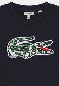Felpa blu navy di Lacoste con un grande logo rettile in bianco, verde e rosso, caratterizzato da motivi geometrici. Realizzata in morbido cotone.
