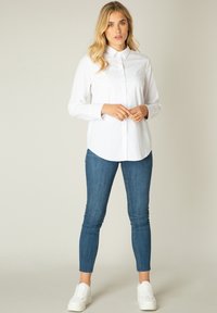 Witte overhemd met kraag, lange mouwen en een gebogen zoom, gecombineerd met blauwe skinny jeans en witte sneakers. Gladde stofstructuur.