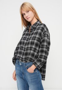 Camisa de franela a cuadros negros y grises con cuello, mangas largas y botones al frente, combinada con vaqueros de mezclilla azul claro. Textura suave.