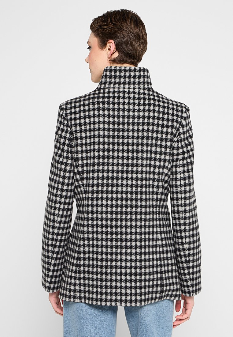 Zwart-wit geblokte blazer met een hoge kraag en een relaxte pasvorm. Heeft een gestructureerde stof en lange mouwen, gestyled met blauwe jeans.