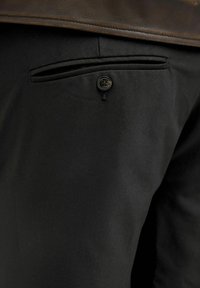 Black trousers with a smooth texture, featuring a back pocket with a single black button. The fabric appears lightweight and tailored.