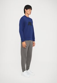 Felpa blu con logo nero, pantaloni della tuta grigi e sneakers bianche. Il tessuto sembra morbido, con scollo rotondo e polsini a costine.