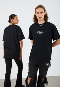 Black oversized t-shirt with a butterfly logo and "FLIGHT" text on the front. Model is paired with distressed black jeans and flared leggings.