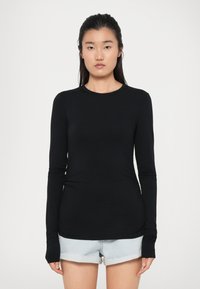 Top nero a maniche lunghe realizzato in un tessuto morbido, con scollatura rotonda e design aderente, abbinato a pantaloncini di jeans azzurri.
