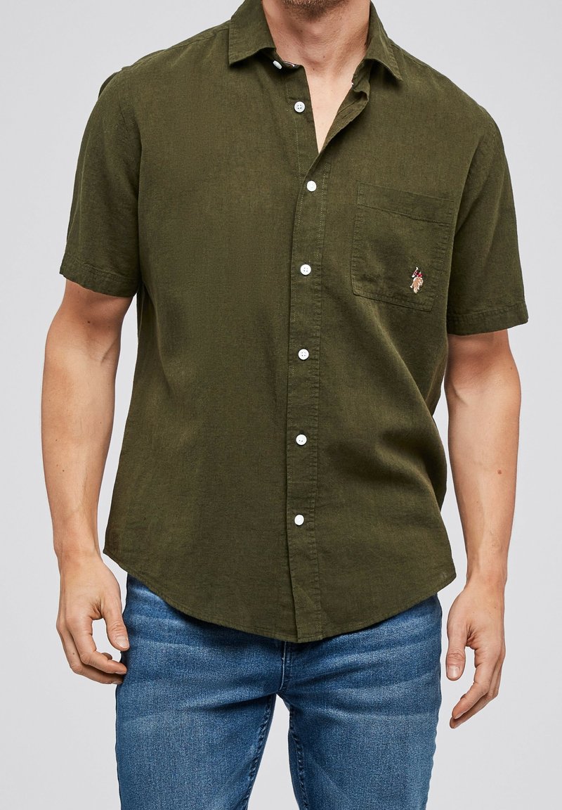 Camicia a maniche corte di colore verde oliva in tessuto leggero, con chiusura a bottoni frontale, taschino sul petto e piccolo dettaglio ricamato.