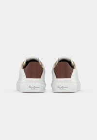 Sneaker bianchi con dettagli in pelle marrone sul tallone, materiale superiore liscio e suola in gomma bianca con marchio sul lato.
