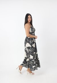 Robe maxi noir et blanc avec motif de feuilles, corsage ajusté, bretelles spaghetti et ourlet froncé. Associée à des sandales à talons hauts argentées.