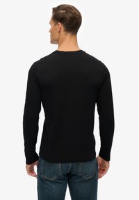 Zwarte longsleeve t-shirt van zacht materiaal, met een ronde hals en een fitted snit. Draagt het met blauwe jeans, toont een eenvoudig ontwerp.