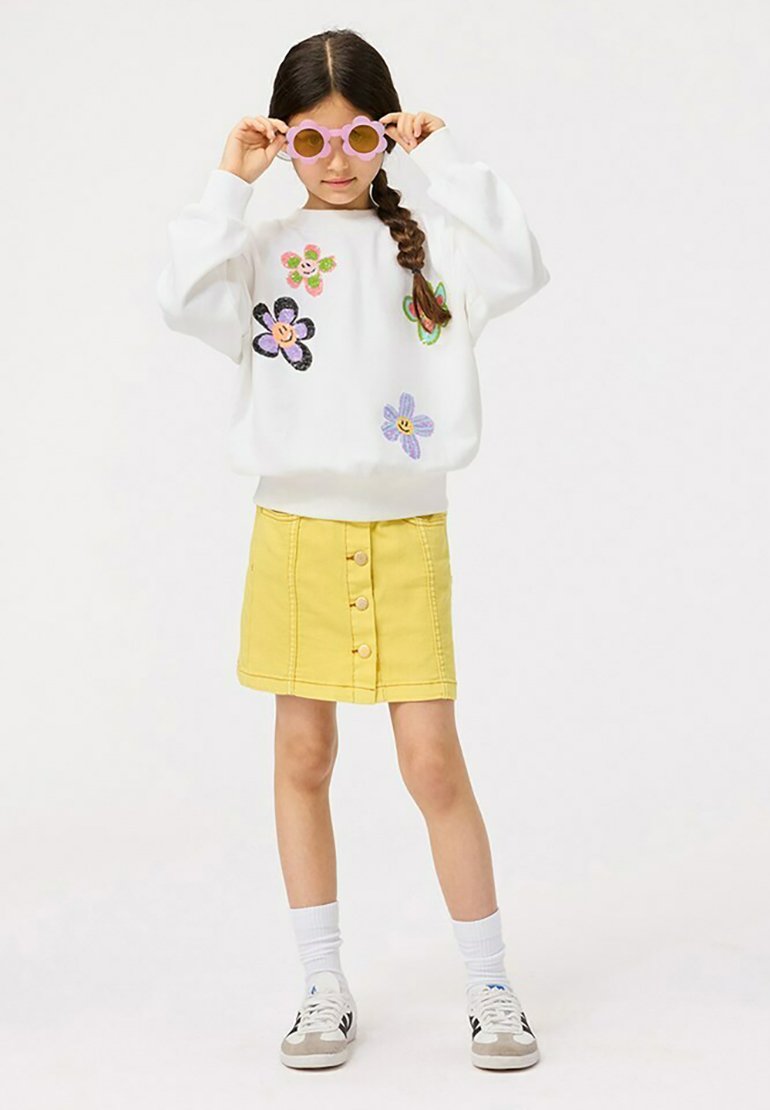 Witte sweatshirt met kleurrijke bloemenborduursels, gecombineerd met een gele denimrok met knopen aan de voorkant. Accessoires zijn onder andere ronde roze zonnebrillen.