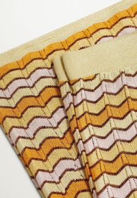 Tissu tricoté avec un bord plié, présentant un motif en zigzag dans des tons jaunes, orange, beige et marron sur un fond clair.