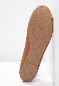 Chaussure en cuir brun clair avec une semelle flexible, ornée d'un motif paisley et d'accents en relief. Taille indiquée comme 42 au fond.