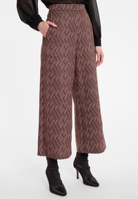 Pantalons larges en tissu marron avec un motif géométrique de lignes rouges et blanches. Comprend des poches latérales et une taille haute.