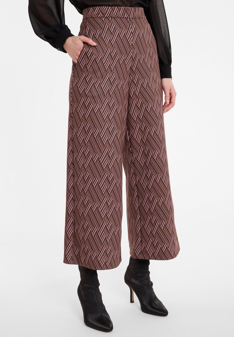 Pantalons larges en tissu marron avec un motif géométrique de lignes rouges et blanches. Comprend des poches latérales et une taille haute.