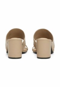Beige Absatzsandalen mit offenem Fersenbereich, ausgestattet mit überkreuzten Riemen und einem breiten Absatz. Sanfte Lederoberfläche und minimalistisches Design.