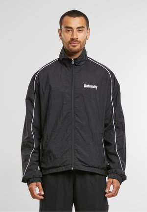 Black windbreaker jacket with a high collar, zip closure, and white striped accents along the shoulders. Features the word "Reternity" in white.