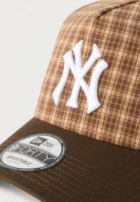 Καφέ καρό μπέιζμπολ καπέλο με λευκό κεντημένο λογότυπο. Διαθέτει δομημένο μπροστινό μέρος, ρυθμιζόμενο λουράκι και στρογγυλεμένη γείσο.