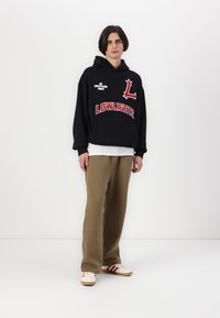 Black hooded sweatshirt with red graphics, beige wide-leg pants, and white sneakers with red stripes. Simple design and casual fit.