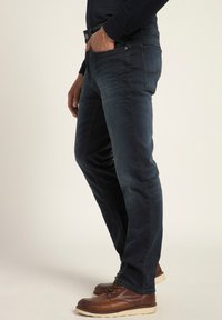 Jeans de mezclilla azul oscuro con corte recto, cinco bolsillos y un ligero desvanecimiento; combinados con zapatos de cuero marrón y una blusa azul marino.