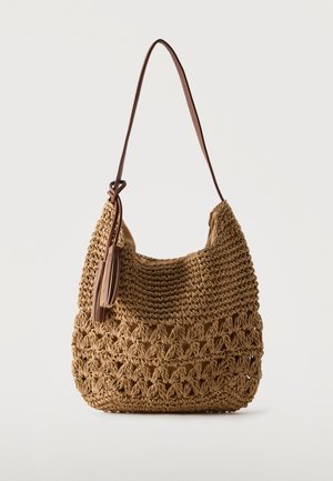 Sac à épaule marron tissé avec une sangle en cuir et un détail pompon, présentant un motif crocheté ajouré sur la moitié inférieure.
