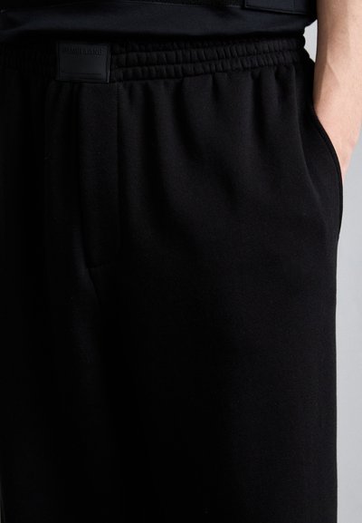 Schwarze Sweatpants aus weichem Material, mit einem elastischen Bund, seitlichen Taschen und einem dezenten Logoetikett auf der Rückseite.