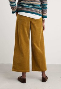Wide-leg corduroy pants in a mustard yellow hue, featuring a ribbed texture, back pockets, and paired with brown slip-on shoes.