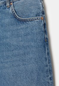Tissu en denim bleu avec poche avant et rivets en cuivre, montrant les coutures détaillées et la texture du matériau jean.