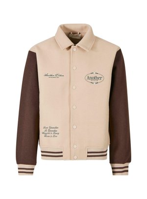 Beige and brown jacket with a button front, collared neck, embroidered text, and striped cuffs. Made of soft fabric, featuring decorative patches.