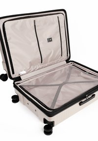Valigia rigida da cabina aperta, che mostra un interno beige con scomparti con cerniera, divisorio in rete, bordatura nera e quattro ruote piroettanti.