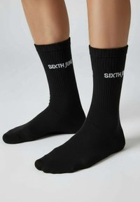 Chaussettes noires en coton avec une texture côtelée, portant le texte blanc "SIXTH JUNE" sur le côté extérieur. Forme et coupe standards.
