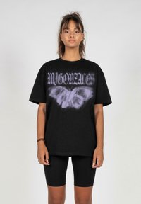 Svart bomull t-skjorte med oversized passform, med grafikk av en lilla sommerfugl og stilisert tekst, sammen med svarte sykkelshorts.
