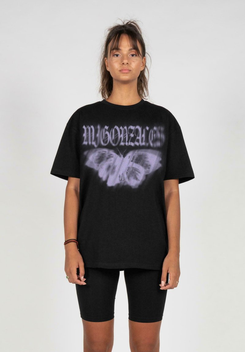 Svart bomull t-skjorte med oversized passform, med grafikk av en lilla sommerfugl og stilisert tekst, sammen med svarte sykkelshorts.