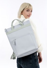 Lichtgrijze leren rugzak met groene stoffen straps, vierkante vorm, ritssluiting, voorvak en een gladde textuur.