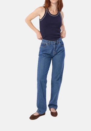 Canottiera blu navy con bordino bianco; jeans a vita alta blu; ballerine marroni senza lacci. L'outfit presenta una vestibilità rilassata e un tessuto denim classico.