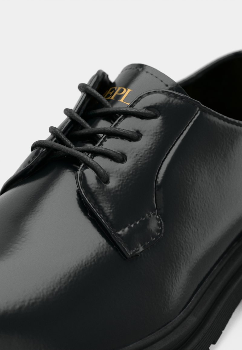 Zapato de vestir de charol negro con un acabado suave, que presenta cordones negros, puntera redondeada y un logo dorado en el costado.