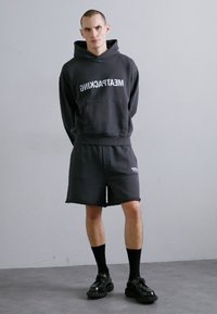 Svart hettegenser med "MEATPACKING" i hvit tekst, kombinert med sorte shorts. Brukt med svarte sokker og kraftige svarte sko. Minimalistisk design.