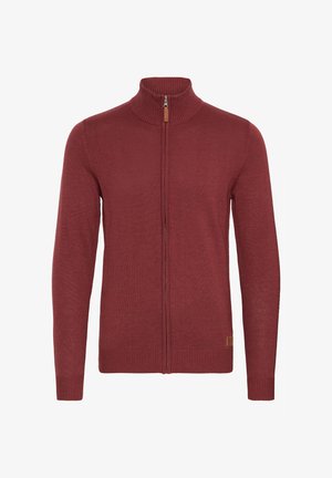Czerwony sweter na zamek z wysokim kołnierzem, ściągaczami u dołu rękawów i na dole. Dzianinowa tekstura, z małym skórzanym akcentem w pobliżu suwaka.