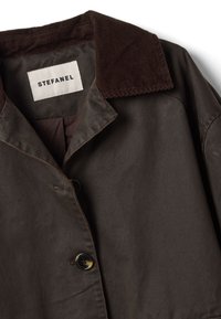 Brauner Baumwollmantel mit einem Cord-Kragen; verfügt über einen einzelnen Knopfverschluss und sichtbare Nähte. Das Etikett trägt die Aufschrift "STEFANEL".