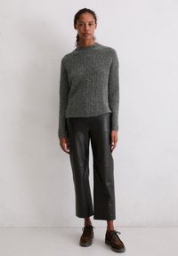 Grauer strukturierter Strickpullover mit langen Ärmeln und Rundhalsausschnitt, kombiniert mit schwarzen Leder-Cropped-Hosen. Die Schuhe sind braune Schnürschuhe.
