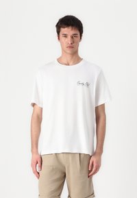 Witte katoenen t-shirt met een ronde hals, korte mouwen, voorzien van een klein zwart "Country Club" logo op de linkerkant van de borst.