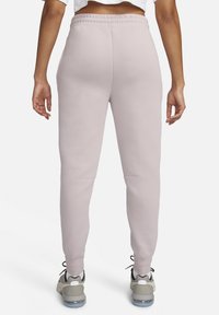 Pantaloni sportivi rosa chiaro a vestibilità slim, realizzati in tessuto morbido, con vita elastica e tasche laterali. Indossati con scarpe da ginnastica grigie.