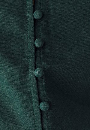 Zielony materiał o gładkiej fakturze, z równomiernie rozmieszczonymi, okrągłymi, teksturowanymi guzikami wzdłuż krawędzi. Prosty design bez dodatkowych wzorów.