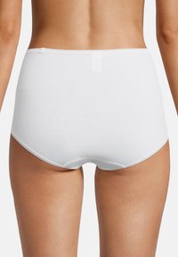 Back of a person wearing high-waisted white cotton underwear with scalloped edges, against a plain background.